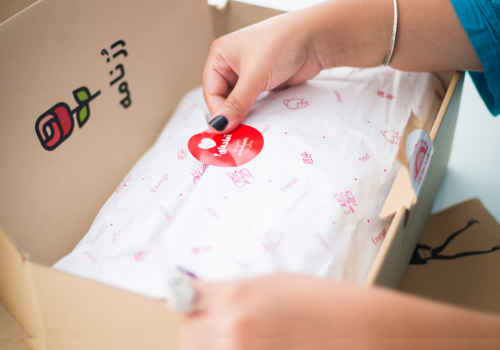 a person sealing a custom package with decorated tissue paper